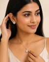Woman wearing a gold necklace and earrings with a neutral background
