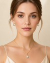 Woman wearing gold necklace and earrings against a beige background