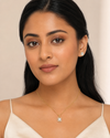 Woman wearing a necklace and earrings against a neutral background