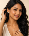 Woman with long dark hair wearing earrings and a necklace against a beige background