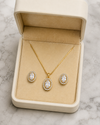 Gold necklace and earrings set in a beige jewelry box on a marble surface