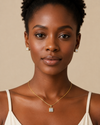 Woman wearing a gold necklace and earrings against a beige background
