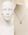 Gold necklace with a square pendant on a mannequin bust, with a white background.