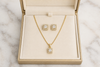 Gold necklace and earrings set in a jewelry box on a marble surface