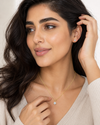 Woman wearing a gold necklace with a diamond pendant, with a plain background