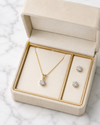 Gold necklace and earrings set in an open jewelry box on a marble surface