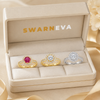 Three rings in a Swarneva box with a pink gemstone, clear gemstone, and silver band.