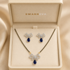 Swarneva Celeste Tie Set in premium jewelry box, silver-tone bow motif necklace and earrings with blue pear stones, necklace 115mm x 90mm and earrings 20mm x 22mm.