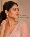 Swarneva Clover Pearl Drops styled on Indian female model in elegant pose, stainless steel gold-tone pearl clover earrings, dimensions 14mm x 14mm.