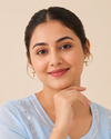 Swarneva Clover Pearl Drops on Indian female model, stainless steel gold-tone clover earrings with pearl-white detailing, dimensions 14mm x 14mm.
