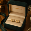 Swarneva gold-tone stainless steel clear stone hoop earrings, 14mm x 14mm, placed in premium jewelry packaging