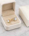 Gold earrings with emerald-cut stones in a beige jewelry box on a marble surface
