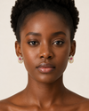 Woman wearing gold earrings with pink gemstones on a beige background