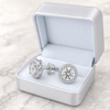 Silver earrings with clear gemstones in a light blue jewelry box on a marble surface