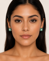 Latina model wearing Swarneva The Valencia Emerald Earring – white gold, white solitaire with green diamond halo, 14x14mm rounded square